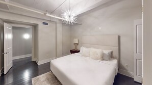A modern bedroom with a large bed, a nightstand with a lamp, a ceiling light fixture, and a door. - 60 Night Minimum Rental - FQ Apt. 2B/2B (New Orleans)