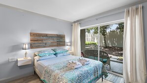 A bedroom with a bed, bedside table, lamp, and a view of the outside. - Just steps to the beach and located within the Sawgrass Beach Club!  (Ponte Vedra Beach)