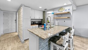 A modern kitchen with granite countertops, white cabinetry, and a built-in island with bar stools. - Just steps to the beach and located within the Sawgrass Beach Club!  (Ponte Vedra Beach)