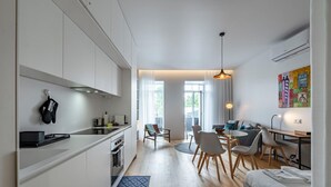 A modern kitchen with white cabinets, a dining area with a round table and chairs, a sofa, and a colorful abstract painting on the wall. - Nomad s Lux - Jardim Vista (Porto)