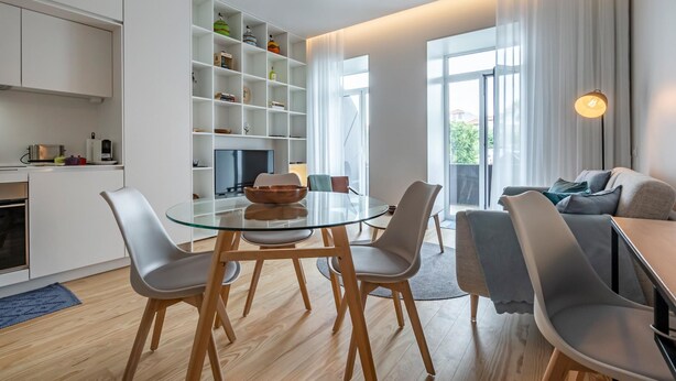 A modern living space with a glass dining table, white cabinetry, and a cozy seating area. - Nomad s Lux - Jardim Vista (Porto)