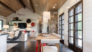 A spacious living area with a dining table, seating, and a stone wall. - 5 Star Luxury, Lake Access, Spectacular Views! (Bryson City)