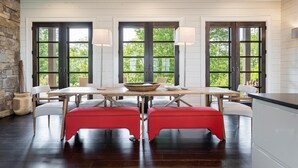 A dining area with a wooden table and red upholstered benches, large windows with dark frames, and a stone wall on one side. - 5 Star Luxury, Lake Access, Spectacular Views! (Bryson City)