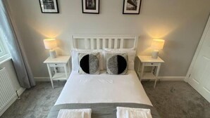 A hotel room with a large bed, two nightstands with lamps, a headboard, and framed pictures on the wall.