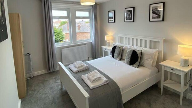 A bedroom with a bed, two bedside tables, a radiator, and a window with curtains.
