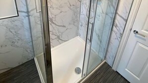 A bathroom with a glass shower enclosure, white marble walls, and a white bathtub.