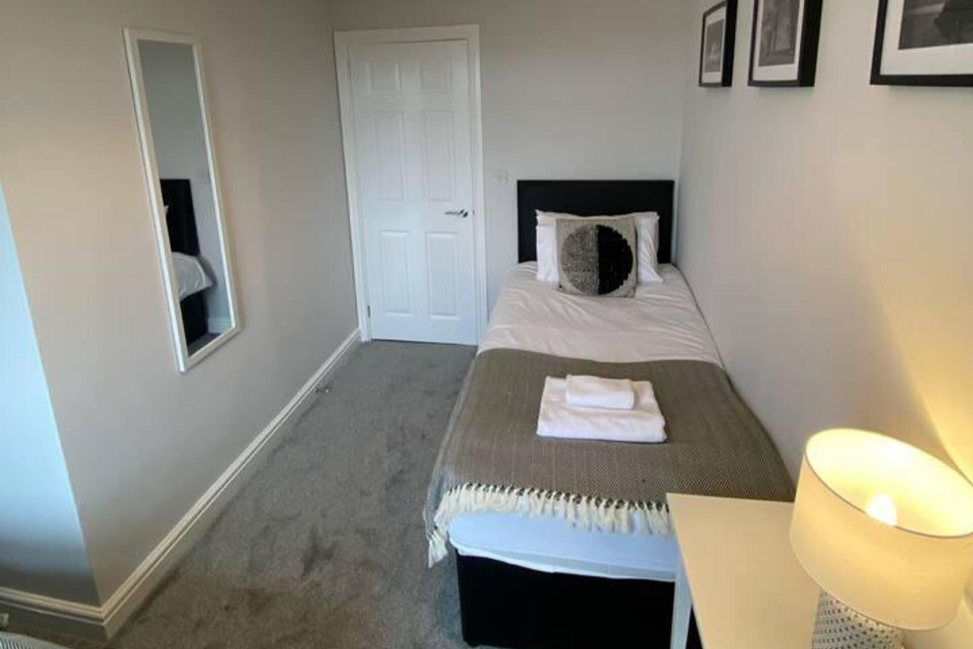 Een hotelkamer met een bed, een bedlamp, een deur en een spiegel.