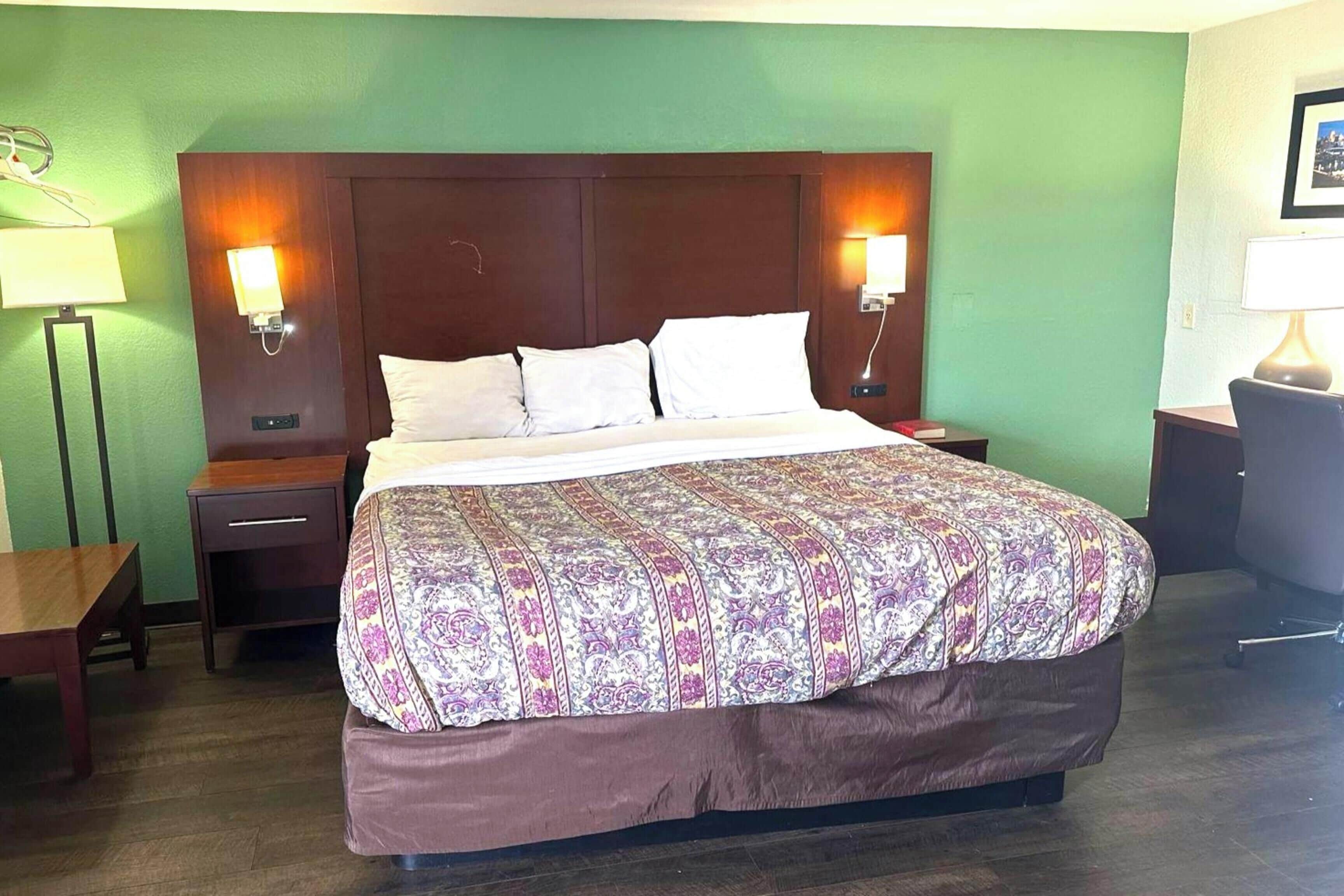 Ein Hotelzimmer mit einem großen Bett, zwei Nachttischen, einem Schreibtisch und einem Stuhl.