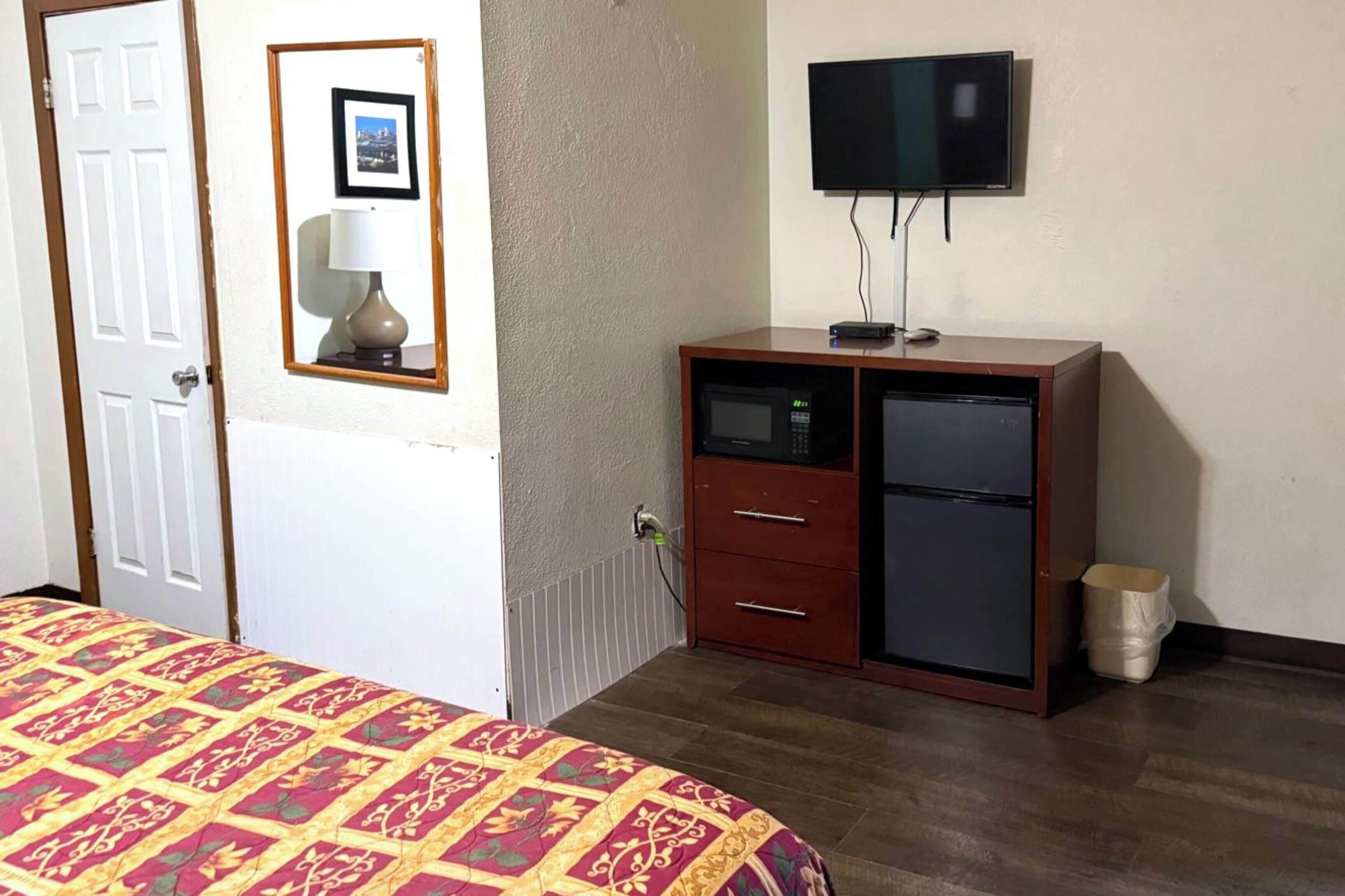 Una habitación con una cama, un armario de madera con televisor, un espejo y un pequeño bote de basura.