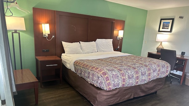 A hotel room with a large bed, wooden headboard, two bedside tables with lamps, a desk with a chair, and a green wall. - Hillcrest Motel By OYO Aurora IN Near Lawrenceburg (Aurora)