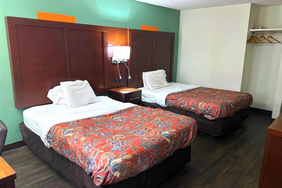 A hotel room with two beds, a wooden headboard, a nightstand, and a wall-mounted lamp.