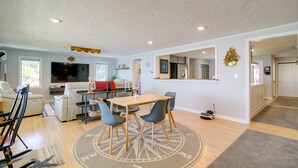A spacious living room with a wooden dining table, blue chairs, and a large TV. - 4 Mi to Downtown Plymouth! Bayfront Home w/ Deck (Plymouth)