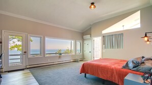 A bedroom with a bed, a desk, and a view of the sea through large windows. - 4 Mi to Downtown Plymouth! Bayfront Home w/ Deck (Plymouth)