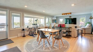 A spacious living area with a dining table, chairs, and a large TV. There are multiple windows providing natural light and a view of the outdoors. - 4 Mi to Downtown Plymouth! Bayfront Home w/ Deck (Plymouth)