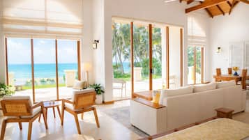 A spacious living area with a large sofa, wooden chairs, and a view of the ocean through large windows.