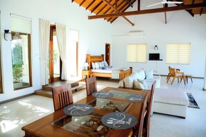 A spacious room with a wooden dining table, a bed with a wooden headboard, a sofa, and a TV mounted on the wall. - Aryan Beach Villa – A Private Family-Friendly Haven in Wadduwa (Wadduwa)