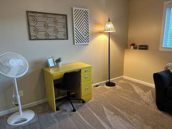 A small office space with a yellow desk, a standing fan, and a floor lamp.