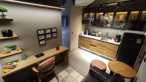 Una cucina funzionale con mobili in legno, un forno a microonde, un lavello e un frigorifero. Alle pareti si notano quadri incorniciati, un tavolino e una sedia.