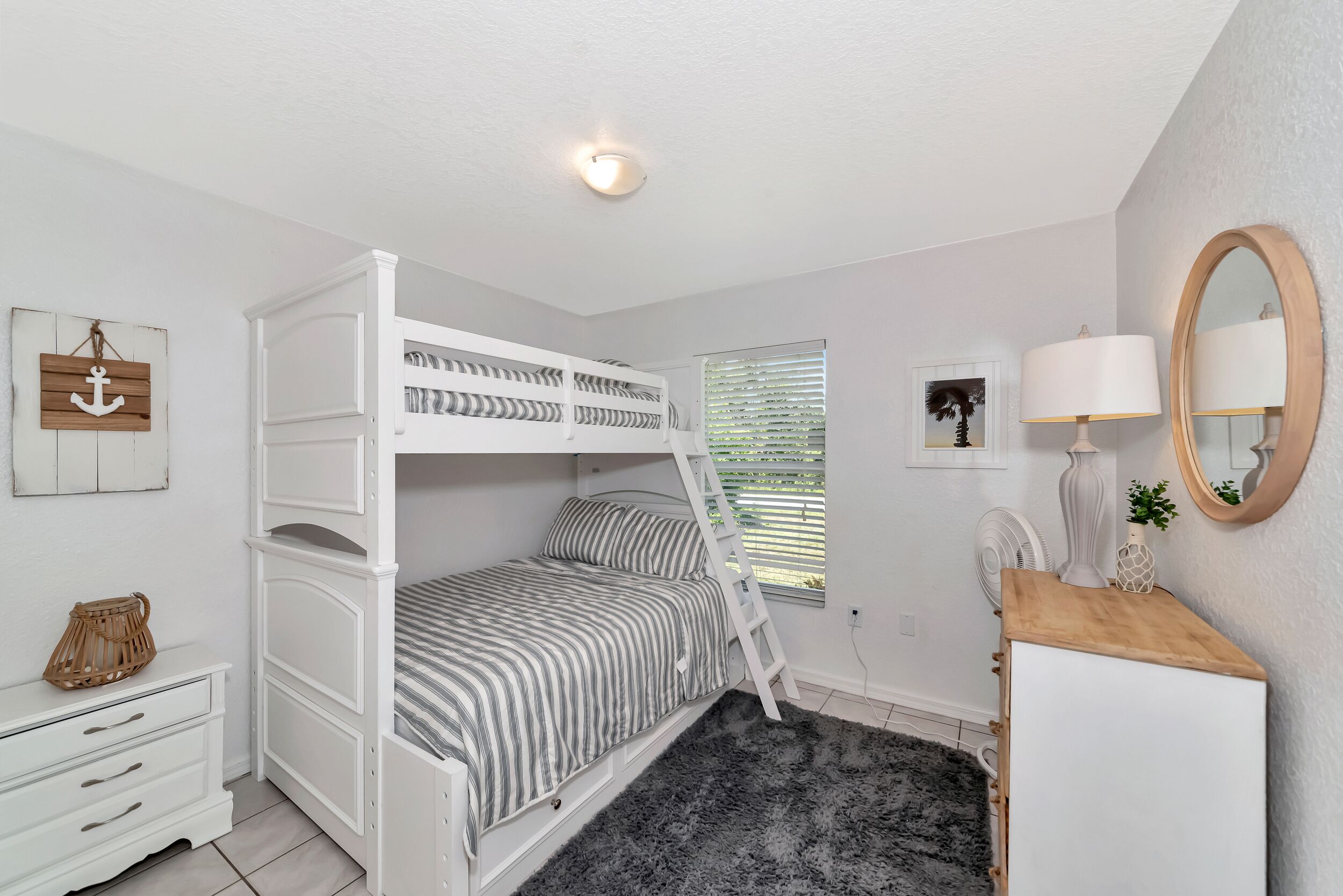 A bunk bed room with a ladder, a dresser, a mirror, and a window with blinds.