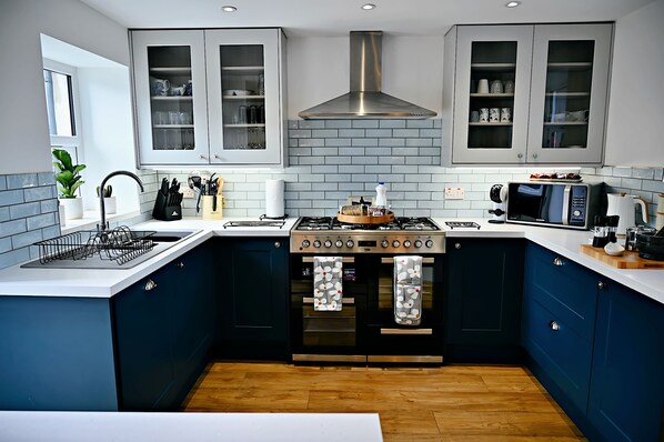 A modern kitchen with dark blue cabinets, a stainless steel range hood, a built-in oven, and a microwave.