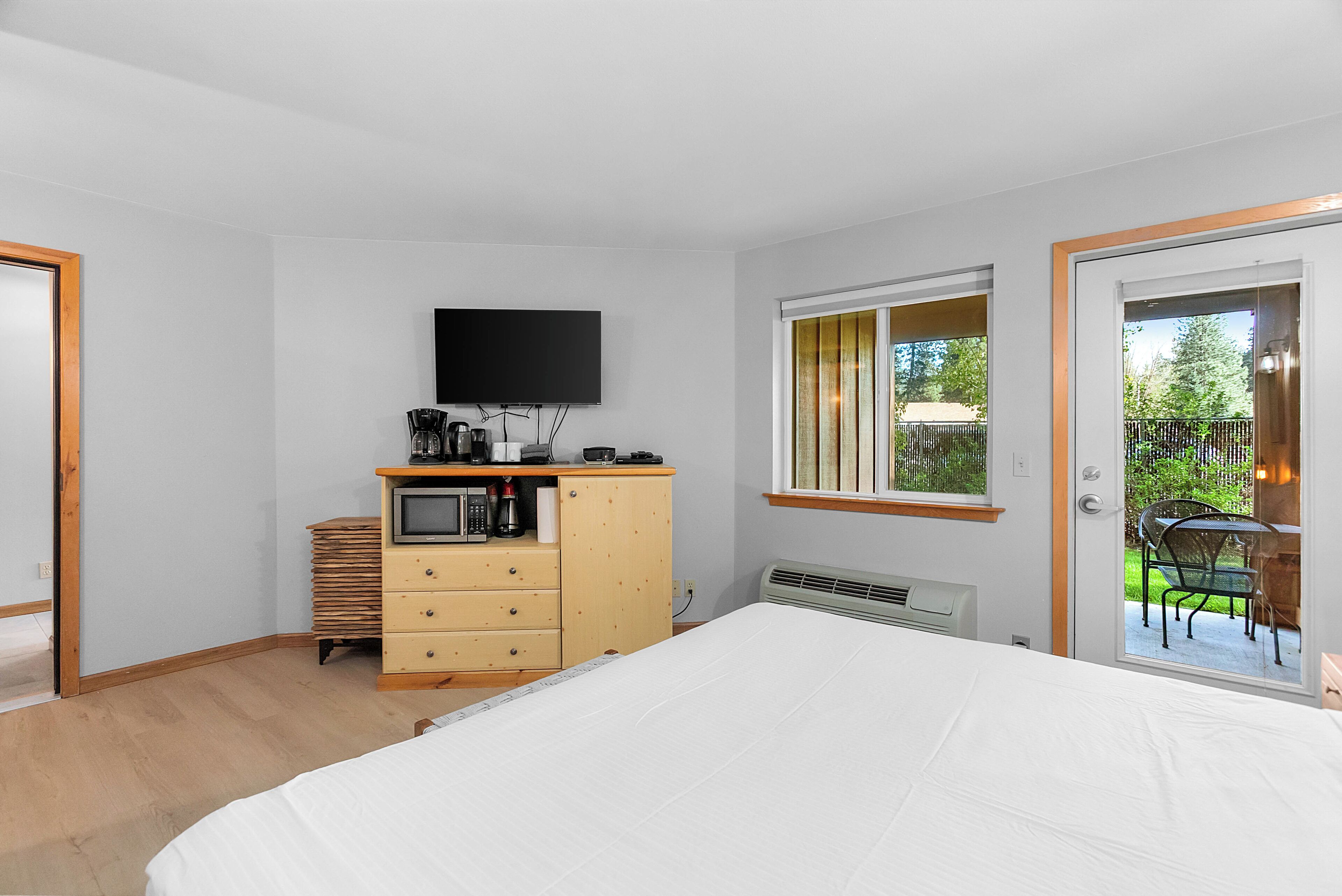 A bedroom with a bed, a TV, a dresser, a microwave, and a window with a view of a garden.