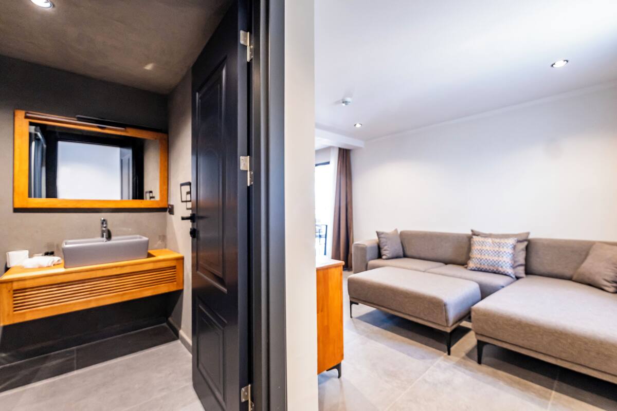 Un baño moderno con una puerta oscura, un tocador de madera y un espejo grande.