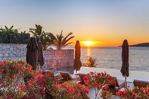 A sunset view from a balcony with lounge chairs and umbrellas, a stone wall, and flowering plants. - Isolina Bodrum (Bodrum)