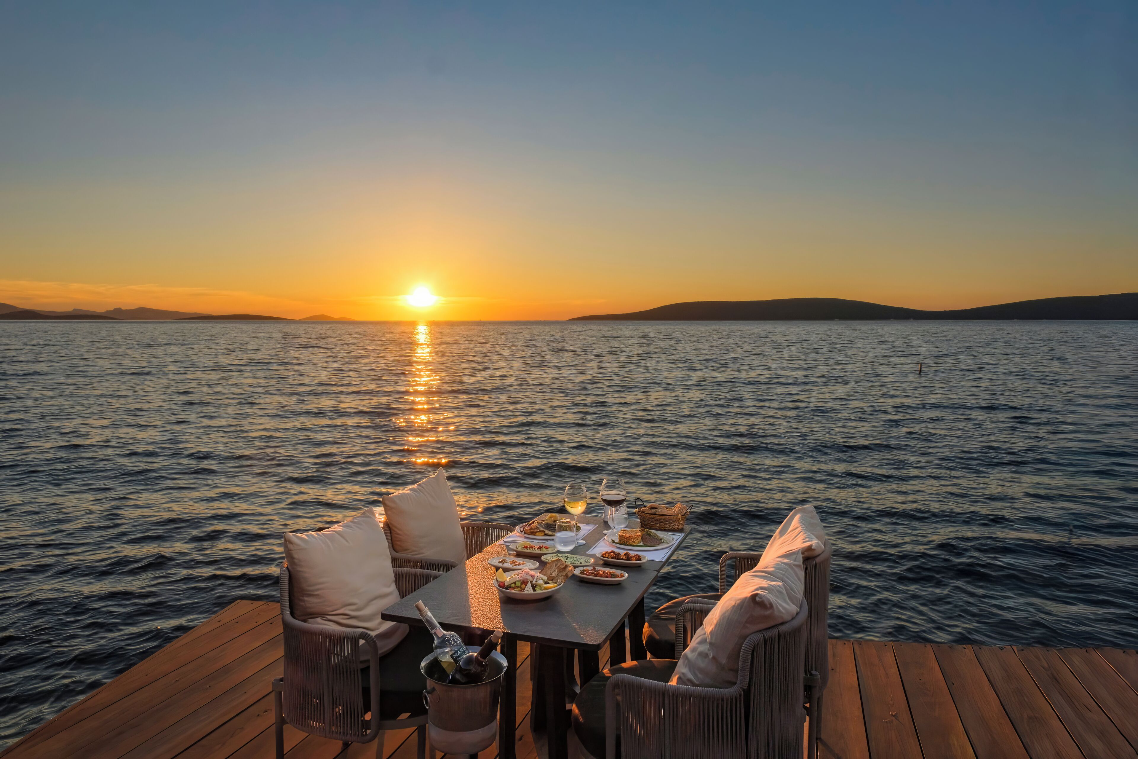 Eine Holzterrasse mit Esstisch, mit Blick auf ein Gewässer bei Sonnenuntergang.
