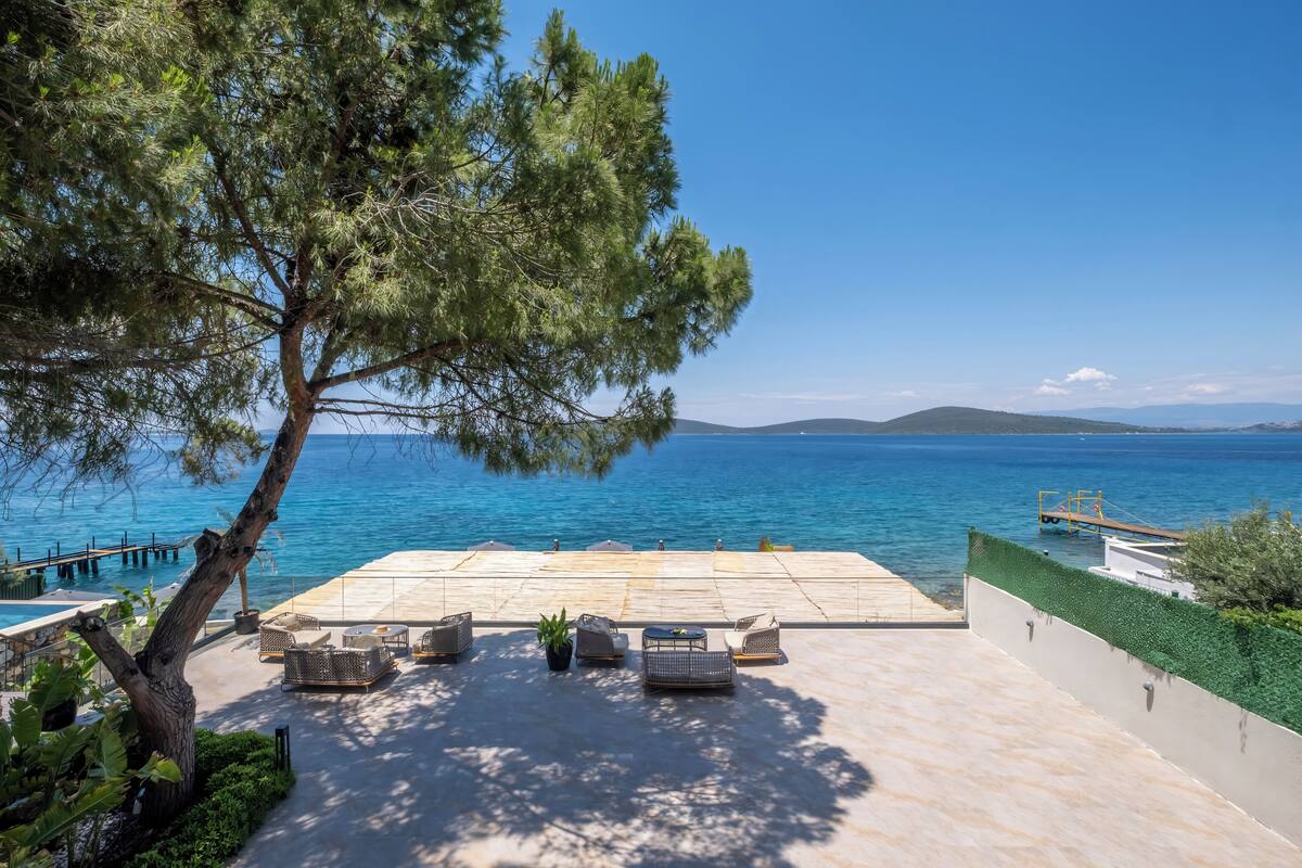 Una terraza con mobiliario exterior que da al mar, un muelle y un cielo despejado.