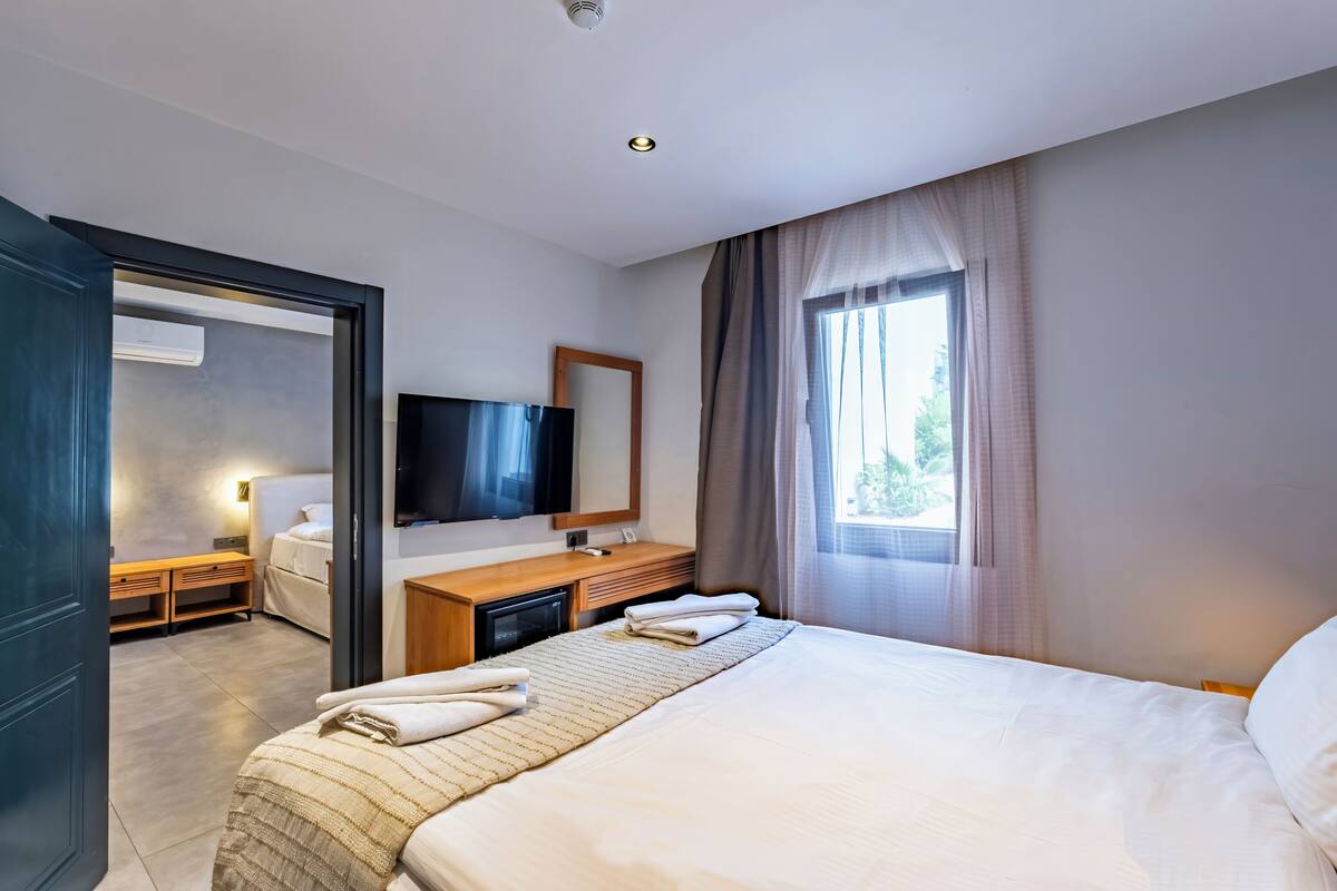 Una habitación de hotel con cama, mesita de noche, televisión y ventana con cortinas.