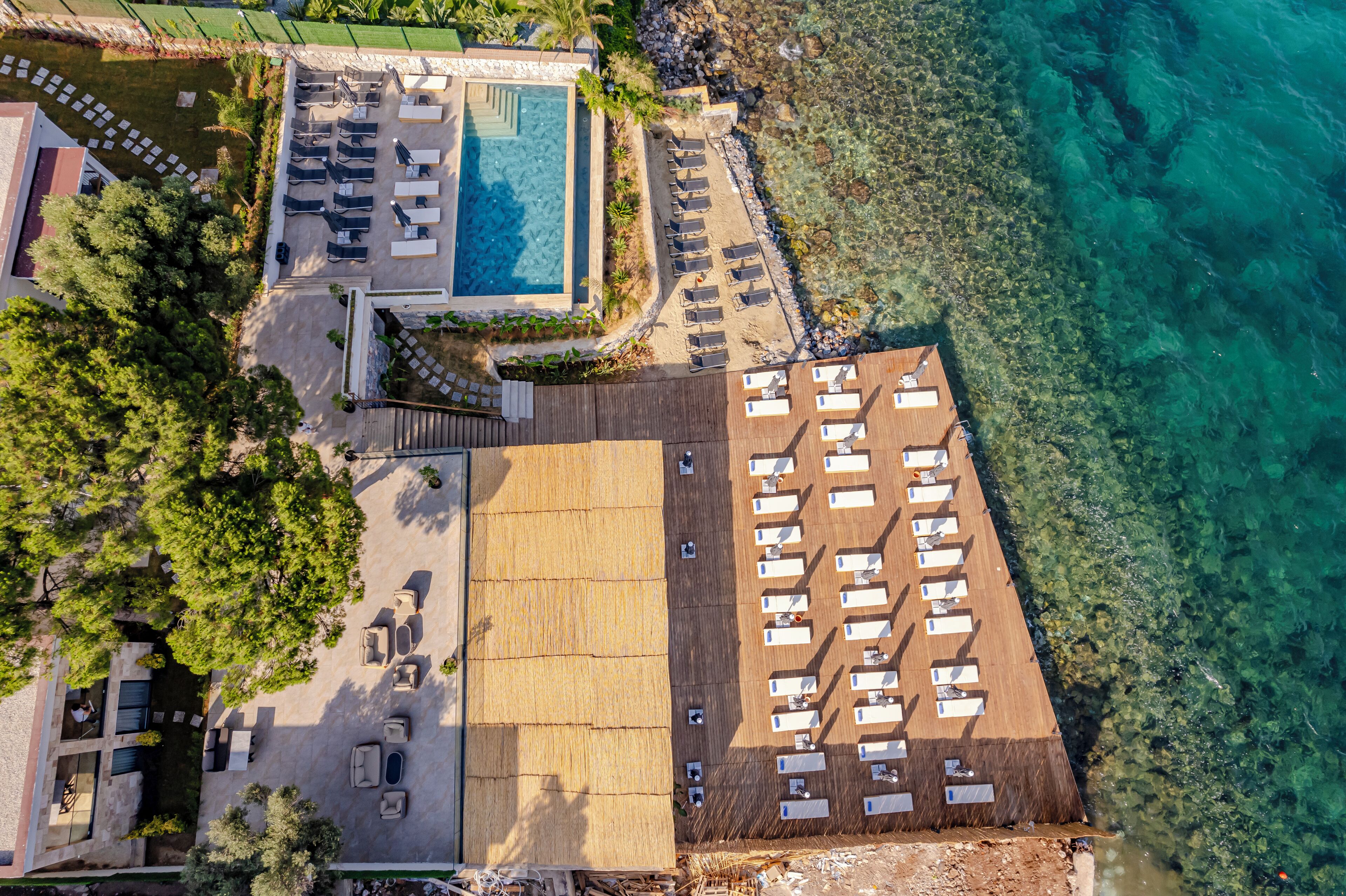 An aerial view of a resort with a swimming pool, sun loungers, and a beach area.