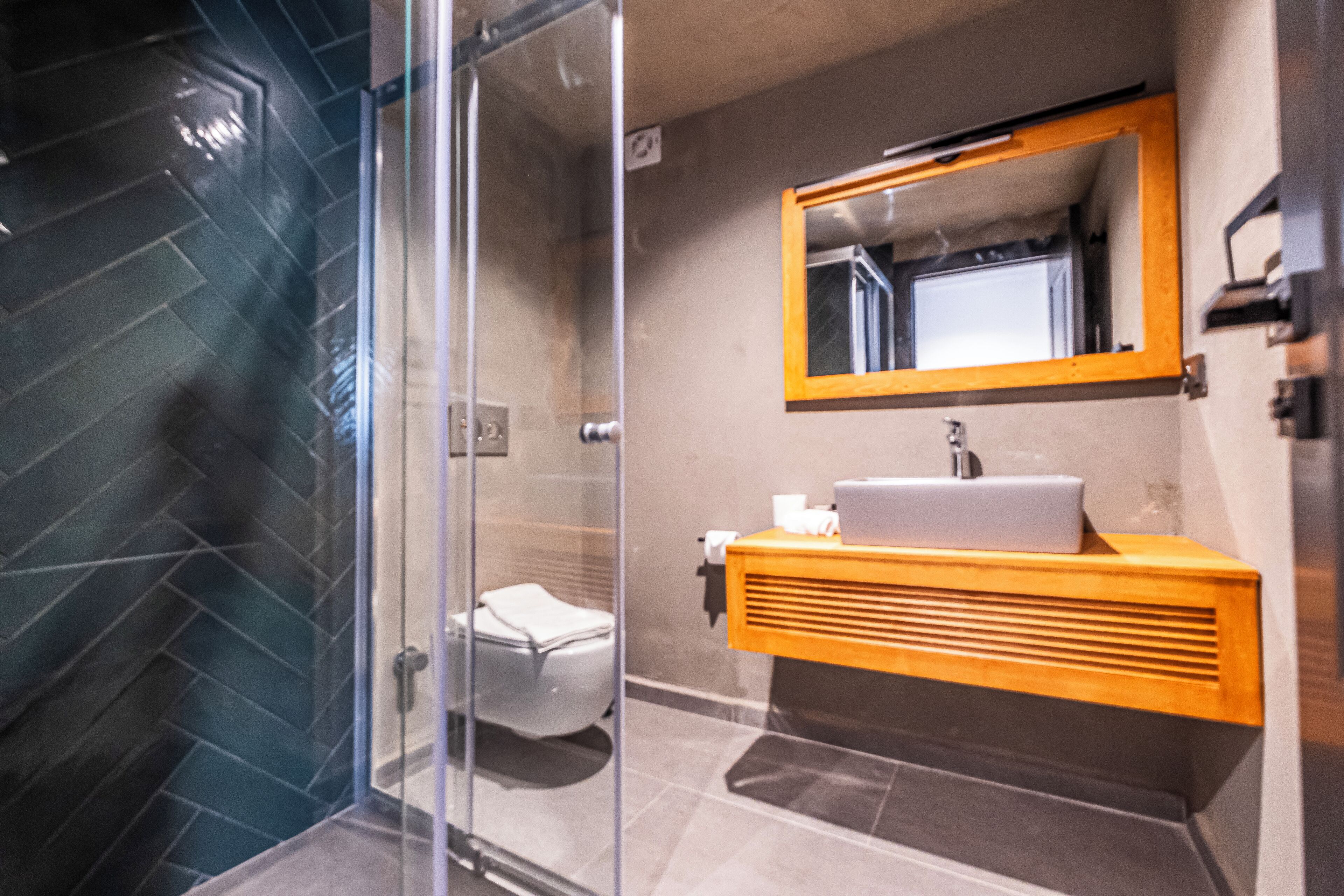 A modern bathroom with a glass shower enclosure, a white sink with a wooden vanity, and a mirror above the sink.
