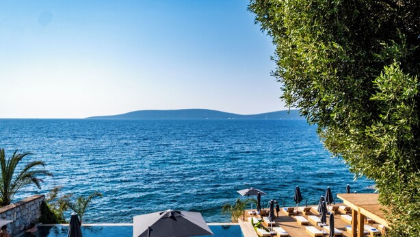 A poolside area with a view of the sea, lounge chairs, umbrellas, and a stone wall. - Isolina Bodrum (Bodrum)