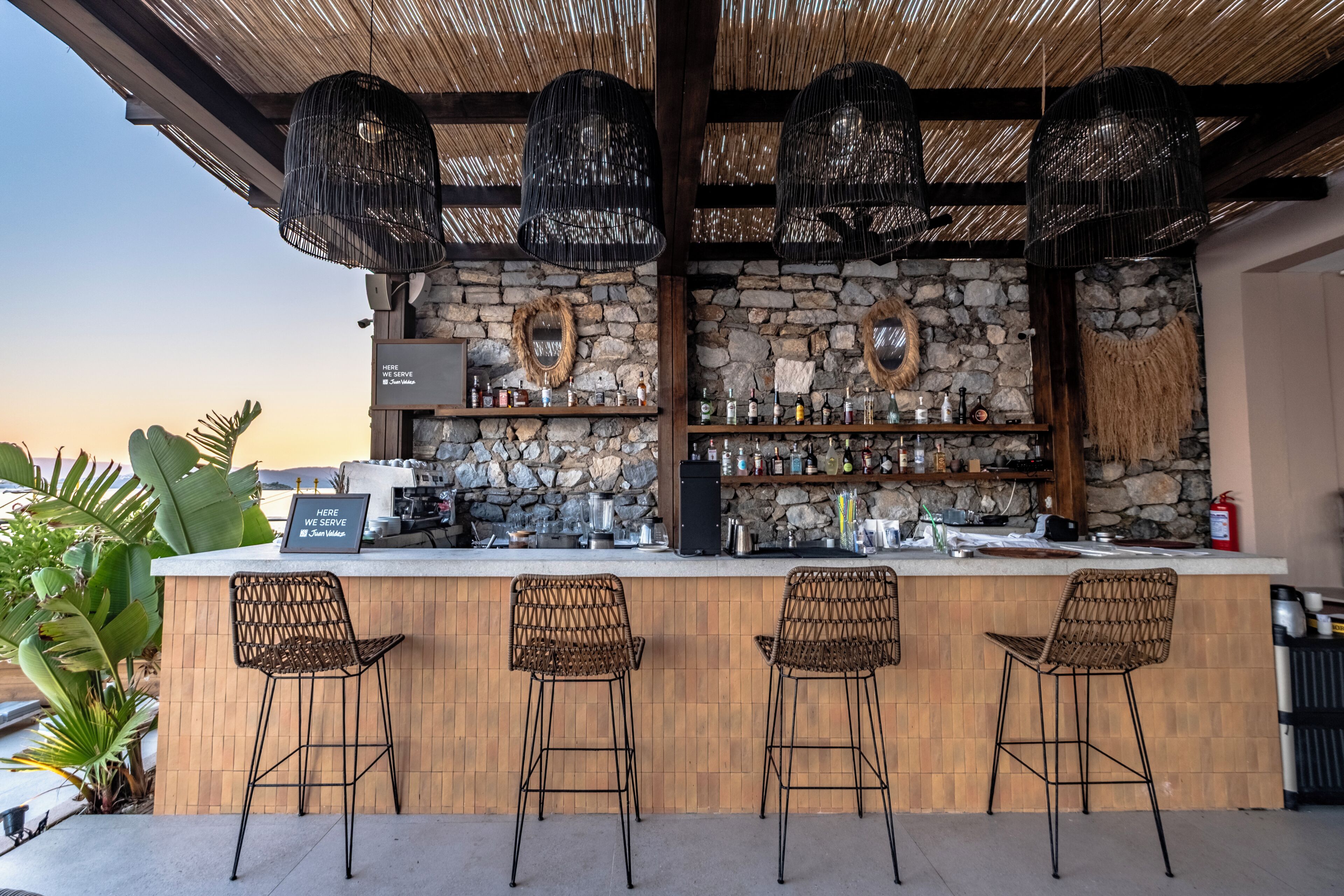 An outdoor bar area with a stone wall, wicker chairs, and hanging lights.