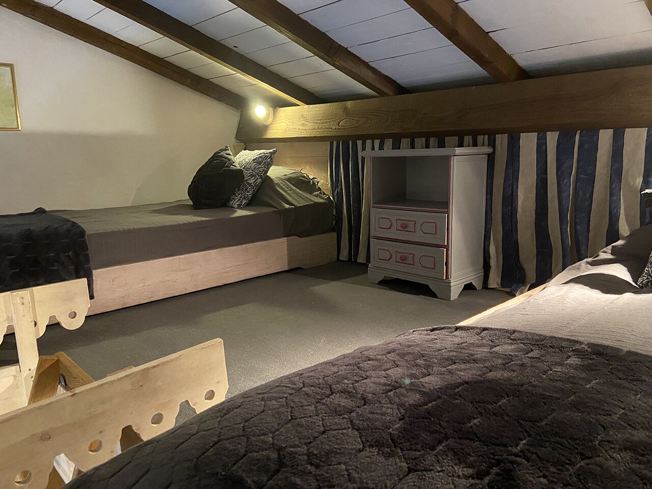 A cozy attic bedroom with a bunk bed, a dresser, and a small seating area.