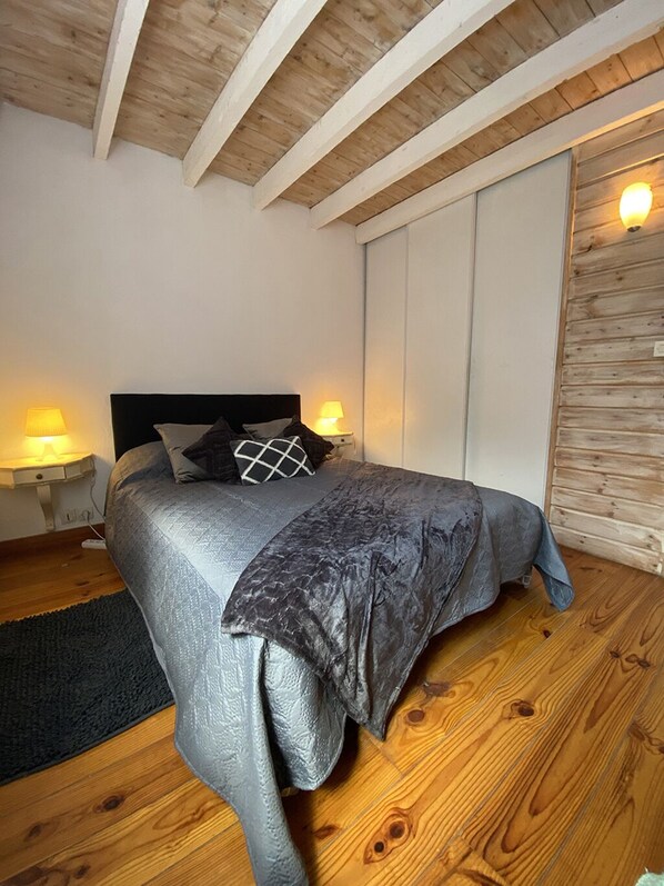 Un dormitorio con una cama, dos lámparas de noche, suelo de madera y techo de madera.