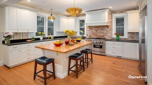Una cocina moderna con armarios blancos, una isla central con taburetes, una pared de acento de ladrillo y un refrigerador de acero inoxidable.