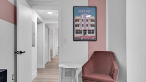 Ein Korridor mit einem gerahmten Poster eines Gebäudes, einem rosafarbenen Sessel und einem kleinen weißen Tisch.