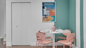 Ein Essbereich mit einem weißen Tisch, gedeckt für vier Personen, rosafarbenen Stühlen und einem Poster von Miami Beach an der Wand.