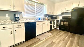 A modern kitchen with white cabinets, a black dishwasher, a coffee maker, a microwave, an oven, and a refrigerator.