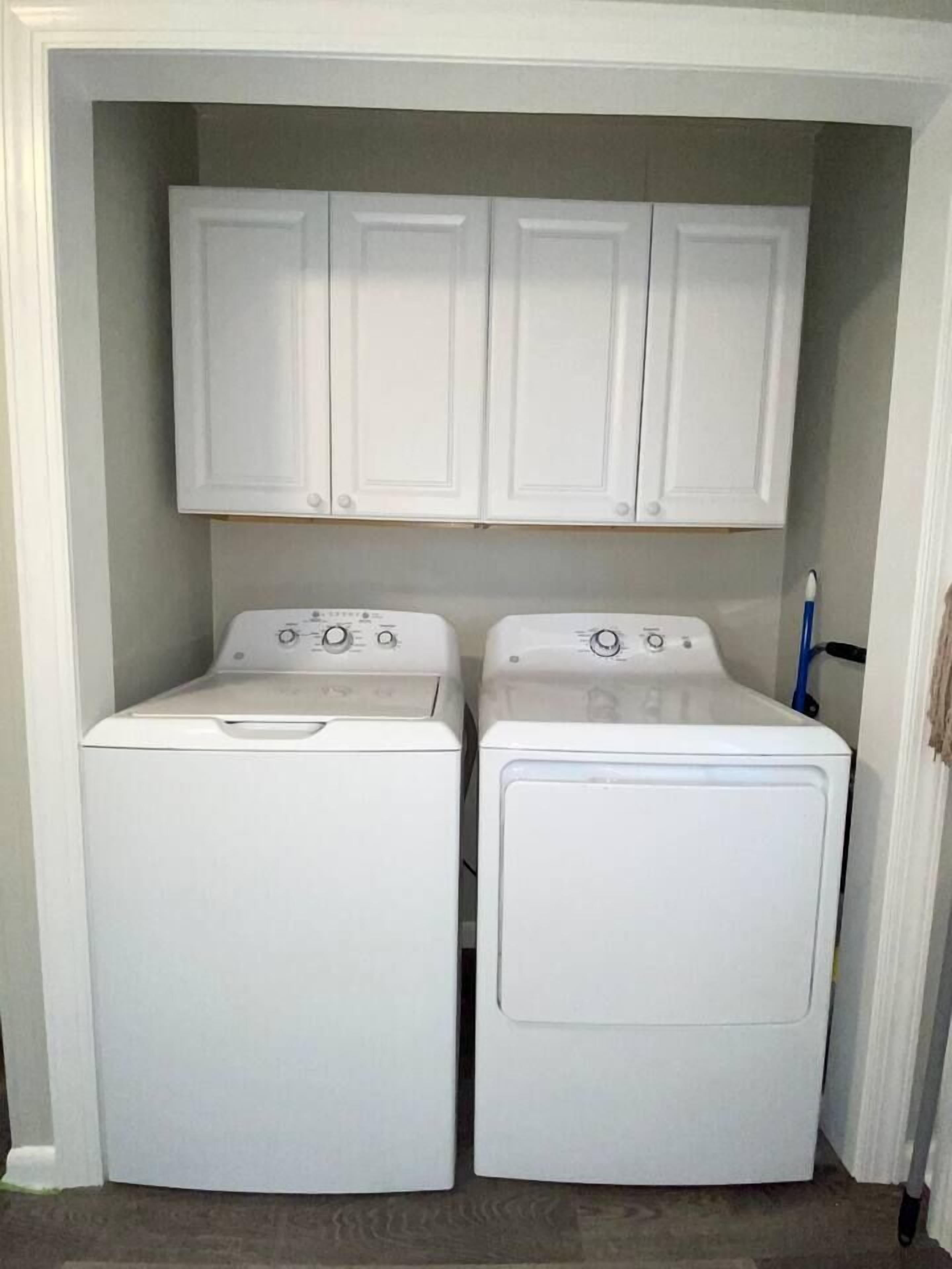 A laundry room with two front-loading washing machines and three cabinets above them.