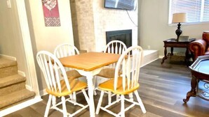 Un comedor con mesa de madera y sillas blancas, chimenea de piedra y televisor montado encima.