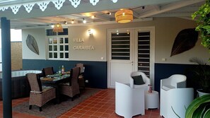 A covered outdoor dining area with wicker furniture, a table with glasses and bottles, and a sign reading 'VILLA CARAIBEA.'