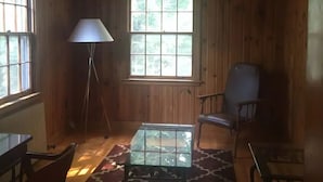 A room with wooden walls, a large window, a glass table, a chair, a lamp, and a radiator. - Windsor Lofts 3 (Roanoke)