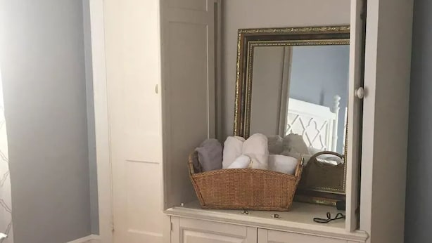 A bedroom with a bed, a white wardrobe, a mirror, and a wicker basket. - Windsor Lofts 3 (Roanoke)