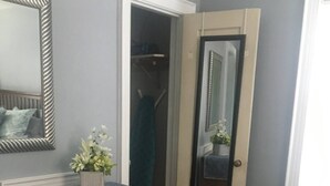 A room with a wooden dresser, a mirror, a chair, and a door leading to a closet. - Windsor Lofts 4 (Roanoke)