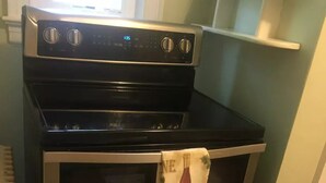 A stainless steel oven with a digital clock display, a wine bottle towel hanging on the oven door, and a white radiator to the left. - Windsor Lofts 4 (Roanoke)