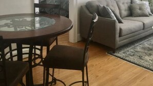A living room with a grey sofa, a glass table, and a wooden floor. - Windsor Lofts 4 (Roanoke)