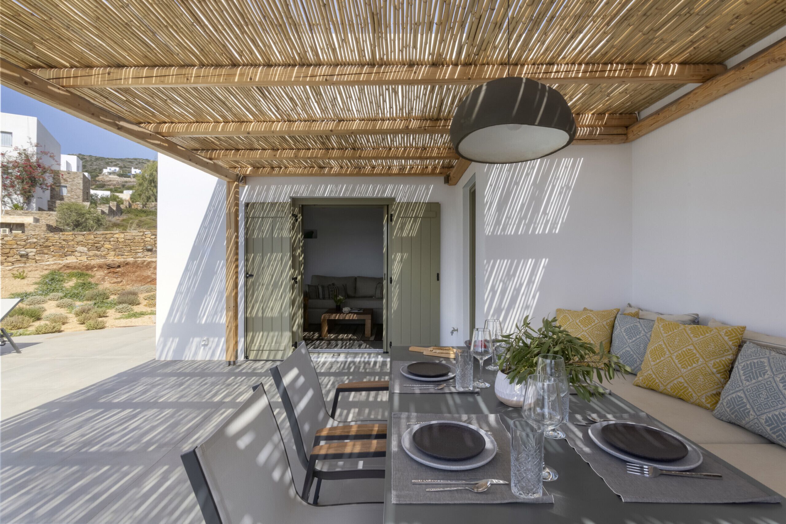 Un área de comedor al aire libre con techo de bambú, una mesa preparada para dos personas y vistas del paisaje circundante.