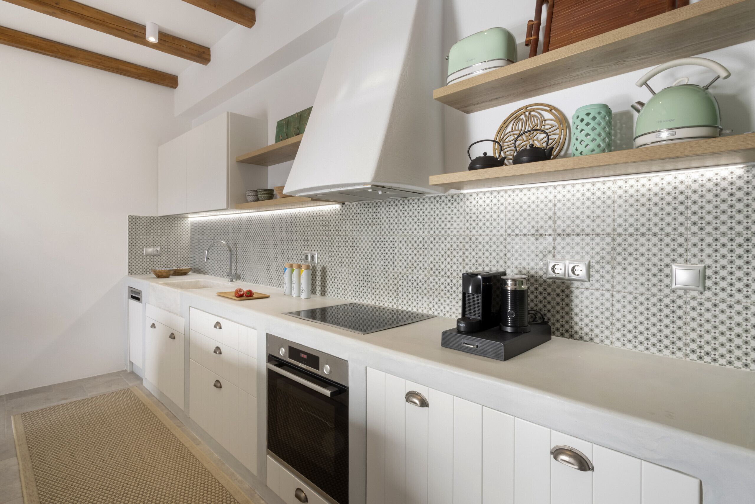 Eine moderne Küche mit weißen Schränken, einem Edelstahlbackofen, einem eingebauten Geschirrspüler und einer Kaffeemaschine auf der Arbeitsfläche.